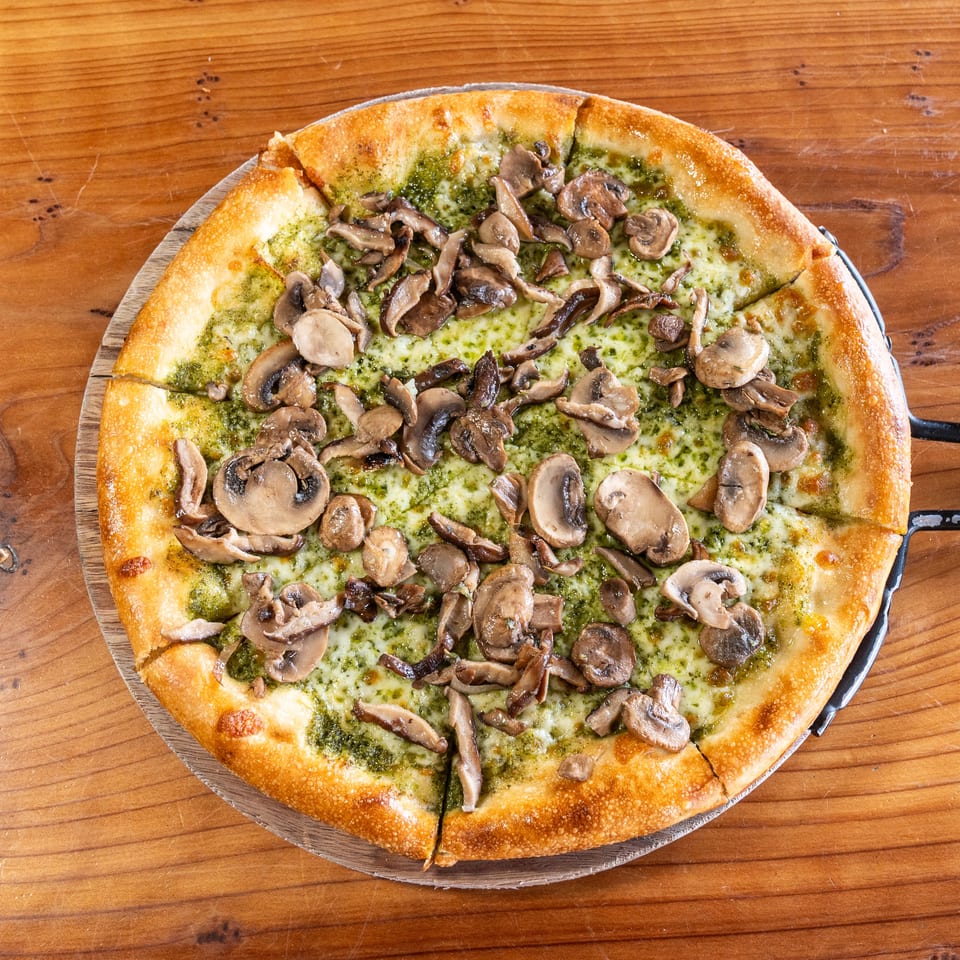Mushroom pizza with pesto, melted cheese, and a golden crust served on a wooden pizza board.