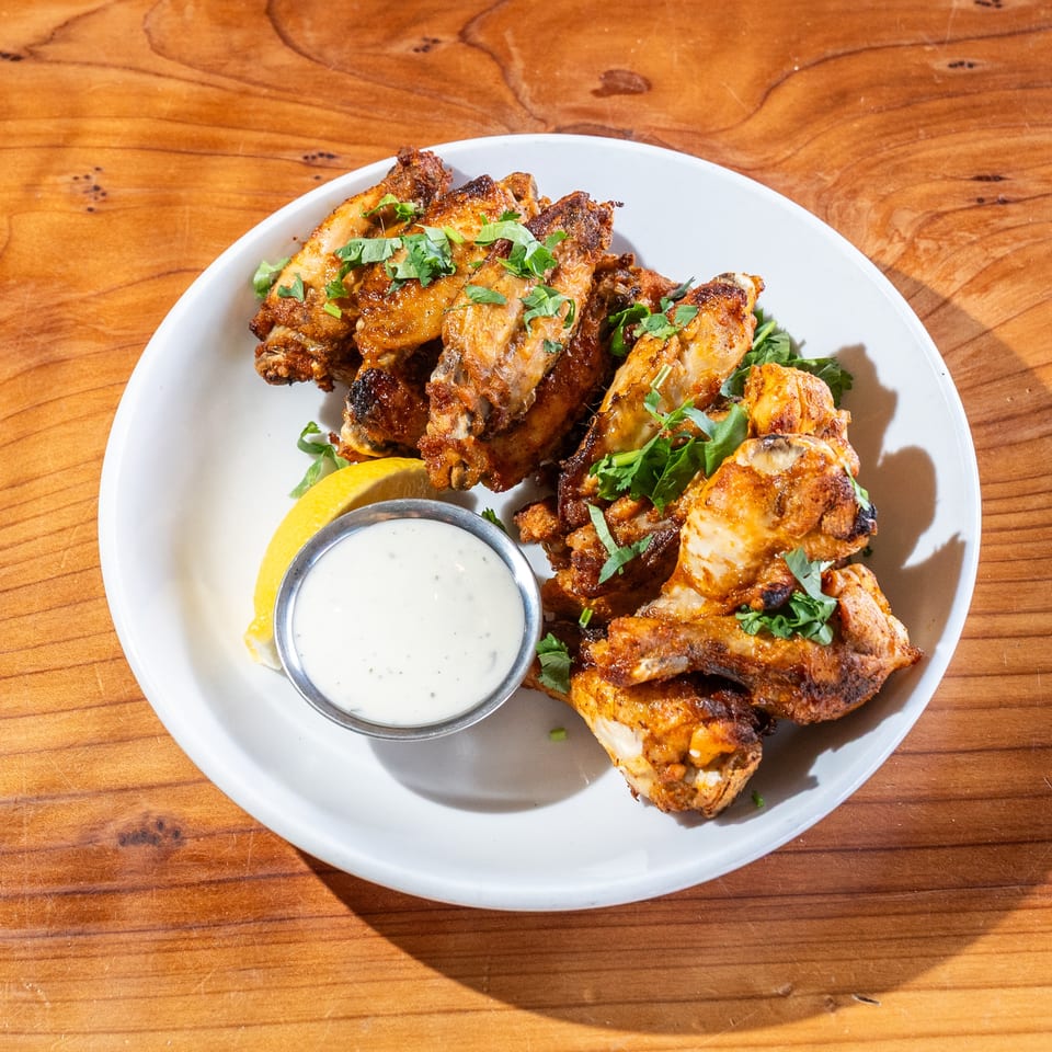 Crispy seasoned chicken wings garnished with herbs, served with lemon and creamy dipping sauce on a white plate.